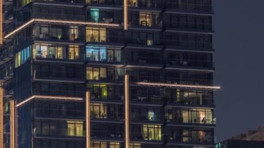 Gece vakitlerinde apartmanların pencereleri, evlerin pencerelerinden gelen ışık. Şehrin akşam manzarası. Balkonlarda insanlar oturuyor.