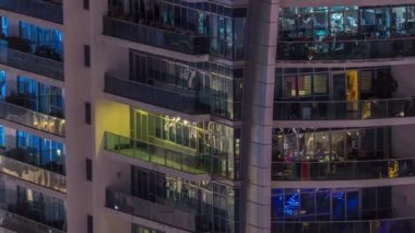 Dışarıdaki apartmanın gece manzarası renkli zaman çizelgesi. Pencerelerinde parlayan ışıklar olan yüksek katlı bir gökdelen. Balkonda sandalyeler