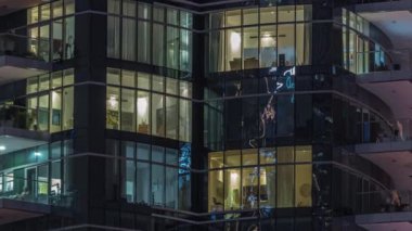 Pencerelerde çok katlı binaların panjurları ve havadan zaman ayarlı düz gece panoraması. Büyük bir şehirde aydınlık bir gökdelen.