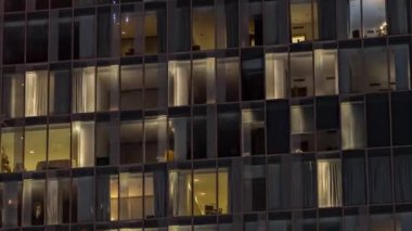 Aydınlatılmış çalışma odası saatleriyle apartman penceresi ön cephesinin gece görüşü. Gökdelende yanıp sönen ışık