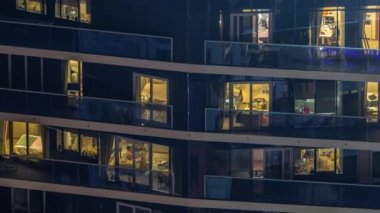 Parlak pencereli, dış apartman manzaralı bir zaman çizelgesi. Yüksek gökdelenler ışıklandırılmış. Balkonlarda gevşeme alanı