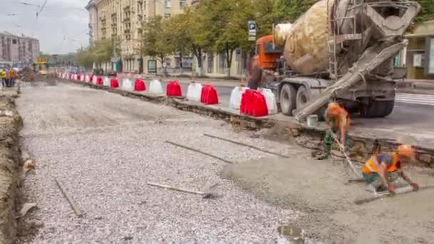 オレンジのユニフォームとミキサーマシンのタイムラプスで多くの労働者と道路建設現場のためのコンクリート工事とレベリング 軌道の再建 — ストック動画