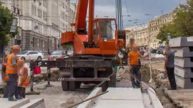 Yol inşaatı zamanına vinçle beton plakalar yerleştiriliyor. Şapkalı ve üniformalı endüstriyel işçiler. Şehir caddesindeki tramvay raylarının yeniden inşası. Bulutlu gökyüzü