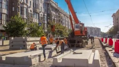 Yol inşaatı zamanına vinçle beton plakalar yerleştiriliyor. Şapkalı ve üniformalı endüstriyel işçiler. Şehir caddesindeki tramvay raylarının yeniden inşası. Mavi açık gökyüzü