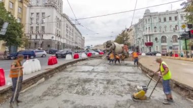 Turuncu üniformalı ve mikser makineli işçilerle yol inşaatı için somut çalışmalar ve sıkıştırma. Tramvay raylarının yeniden inşası