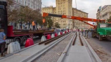 Turuncu inşaat teleskopik mobil vinç kamyon zaman çizgisinden tramvay raylarını boşaltıyor. Şapkalı ve üniformalı endüstriyel işçiler. Evin yakınındaki tramvay raylarının yeniden inşası.