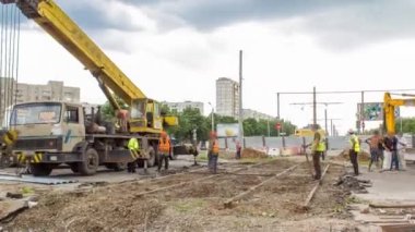 Eski tramvay raylarının yol inşaatında vinçle yıkılması. Şapkalı ve üniformalı endüstriyel işçiler. Şehir caddesindeki tramvay raylarının yeniden inşası