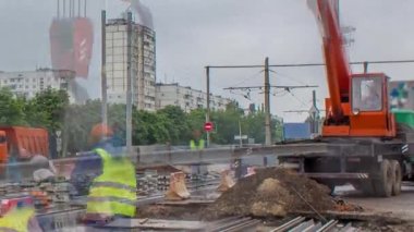 Orange construction telescopic crane unloading tram rails to concrete plates timelapse. Industrial workers with hardhats and uniform. Reconstruction of tram tracks