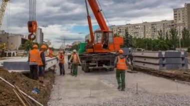 Yol inşaatında vinçle ezilmiş taşın üzerine beton plakalar yerleştiriliyor. Şapkalı ve üniformalı endüstriyel işçiler. Şehir caddesindeki tramvay raylarının yeniden inşası