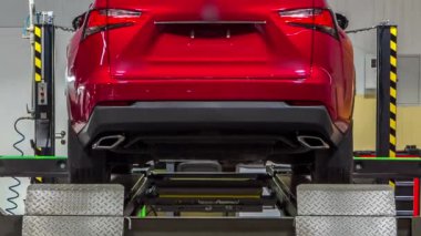 Tekerlek hizalaması için tekerlekli sensörlü araç servis istasyonunun zaman ayarlı atölyesinde kontrol ediliyor. Araba asansörde hareket ediyor