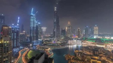 Dubai şehir merkezinden yükselen gökdelenler tüm gece boyunca ışıklar sönerken, alışveriş merkezleri ve çeşmeler modern binalarla çevriliyken gökyüzü bulutlu gökyüzü manzaralı.