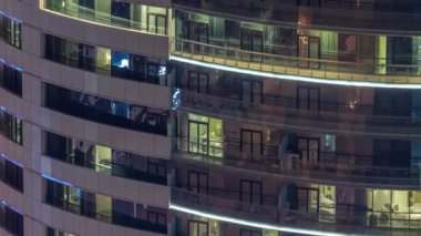 Modern konut binalarındaki büyük parlayan pencereler geceleri zaman ayarlı, sıra sıra parlıyor. Görüntüyü kapat