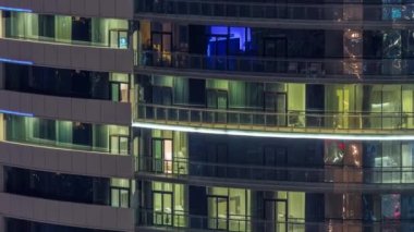 Modern konut binalarındaki büyük parlayan pencereler geceleri zaman ayarlı, sıra sıra parlıyor. Görüntüyü kapat
