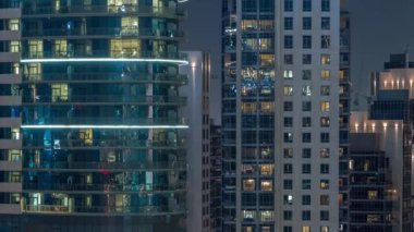 Modern ofisteki büyük parlayan pencereler ve konut binaları gece saatlerine göre ayarlanıyor, pencereler ışık saçıyor. Uzun gökdelenler
