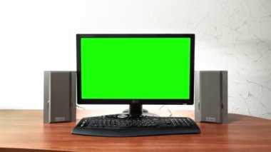 Bilgisayar yeşili ekran monitörü ofisteki bir masanın üzerinde duruyor. Gri ses hoparlörleri ve siyah klavyeli işyeri tasarımı
