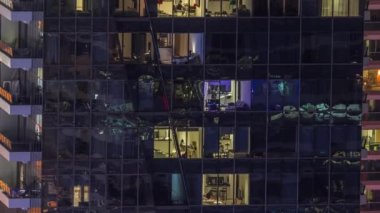 Modern ofisteki pencere ışıkları ve gece vakti balkonlu binalar. İçinde aydınlık odalar olan çok katlı gökdelenler.