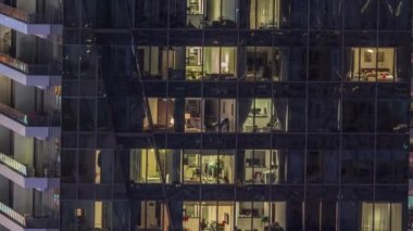 Modern ofisteki pencere ışıkları ve geceleri konut binaları. Çok katlı gökdelenlerin içinde aydınlık odalar ve cam yüzeyden yansımalar var.