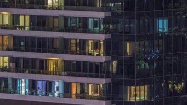 Geceleri modern binalardaki pencere ışıkları zaman ayarlı. İçinde aydınlık odalar olan çok katlı gökdelenler.