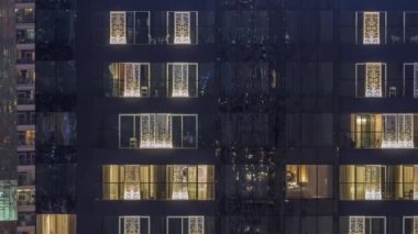 Modern ofisteki pencere ışıkları ve geceleri konut binaları. İçinde aydınlık odalar olan çok katlı gökdelenler. Balkonda birkaç sandalye.