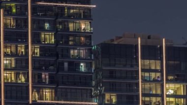 Gece vakitlerinde apartmanların pencereleri, evlerin pencerelerinden gelen ışık. Şehrin akşam manzarası. Balkonlarda insanlar oturuyor.