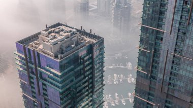 Top view with modern skyscrapers aerial  and water pier of Dubai Marina with morning haze, United Arab Emirates. Yachts and boats between glass towers