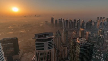 Panorama of Dubai Marina with JLT skyscrapers and golf course during sunrise , Dubai, United Arab Emirates. Aerial view from above towers foggy morning. City skyline with orange sky