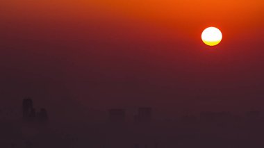 Sunrise close up view over Dubai skyline in the morning, aerial top view from Dubai marina . Big sun on orange sky rise over fog around skyscrapers. United Arab Emirates