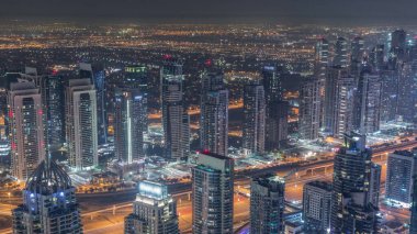 JLT skyscrapers and Dubai marina near Sheikh Zayed Road during all night aerial . Illuminated residential buildings with lights turning off
