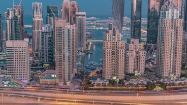Skyscrapers of Dubai Marina with illuminated highest residential buildings night to day transition . Aerial top view from JLT district before sunrise. Yachts floating on water