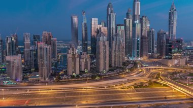 Dubai Marina highway intersection spaghetti junction night to day transition . Illuminated tallest skyscrapers on a background. Aerial top view from JLT district before sunrise