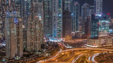 Aerial view on a big highway intersection night  in Dubai Marina with skyscrapers around, UAE. Cars traffic view from JLT district. Illuminated towers with light in windows