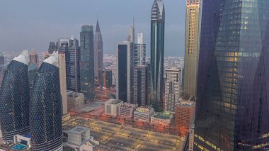 Financial center of Dubai city with illuminated luxury skyscrapers night to day transition , Dubai, United Arab Emirates. Aerial view with parking and towers rooftops