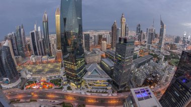 Panorama of futuristic skyscrapers in financial district business center in Dubai with road traffic night to day transition . Aerial view from above with illuminated towers during sunrise