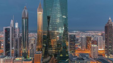 Financial center of Dubai city with illuminated luxury skyscrapers night to day transition , Dubai, United Arab Emirates. Aerial view with light in windows and office towers