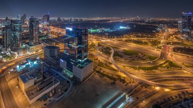 Aerial panoramic view of media city district and highway junction during all night  from Dubai marina with lights turning off. Towers and skyscrapers with traffic on a highway from above