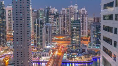 Aerial view on Dubai Marina and JLT illuminated skyscrapers and the most luxury yacht in harbor day to night transition . Towers along walking area on a waterfront. Dubai, United Arab Emirates