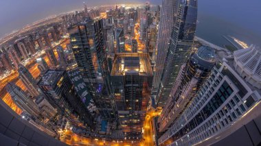 Skyline panorama of Dubai Marina showing canal surrounded by illuminated skyscrapers along shoreline aerial night to day transition . Many tallest towers and traffic on streets during sunrise. DUBAI, UAE