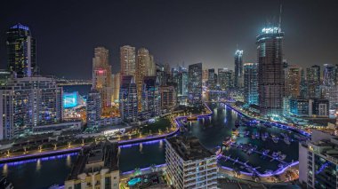 Panorama showing Dubai Marina with several boat and yachts parked in harbor and illuminated skyscrapers around canal aerial night . Towers of JBR district on a background
