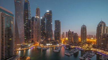 Dubai marina tallest skyscrapers and yachts in harbor aerial night to day transition  during sunrise. View at apartment buildings, hotels and office blocks, modern residential development of UAE