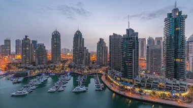 Luxury yacht bay in the city aerial night to day transition  in Dubai marina before sunrise. Modern skyscrapers along waterfront promenade and boats floating in harbor