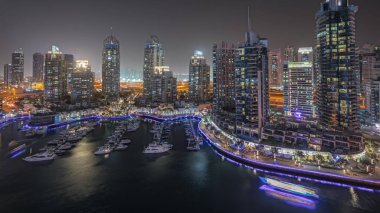 Panorama showing luxury yacht bay in the city aerial night  in Dubai marina. Modern skyscrapers along waterfront promenade and boats floating in harbor