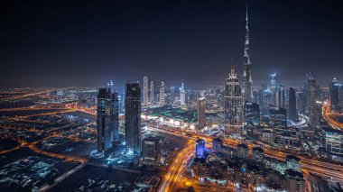 Panorama showing aerial view of tallest towers in Dubai Downtown skyline and highway night  panorama. Financial district and business area in smart urban city. Skyscraper and high-rise buildings