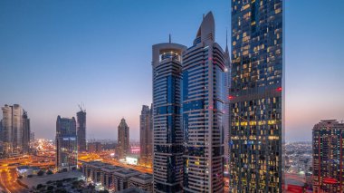 Aerial view of Dubai International Financial District with many skyscrapers day to night transition  after sunset. Traffic on a road junction near parking lot. Dubai, UAE.