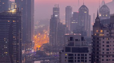 Dubai Marina and Media City districts with modern skyscrapers and office buildings aerial night to day transition . Traffic on overpass and road intersection near yachts in harbor