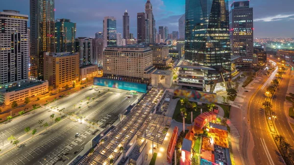 Dubai International Financial district night to day transition . Panoramic aerial view of business office towers and parking lot before sunrise. Illuminated skyscrapers with hotels and shopping mall