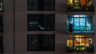 Gece saatlerinde apartmanın pencereleri, balkonunda sandalyeleri olan aydınlık evlerin ışıkları. Gökdelenlerin kentsel manzarası