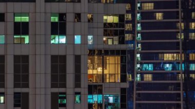 Gece karanlığa bürünmüş gökdelenin panoramik pencereleri şehrin ışıklarının yansımasıyla parlıyor. Aydınlatılmış kuleler