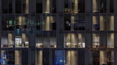 Aydınlatılmış çalışma odaları zaman ayarlı ofis cam pencere cephesinin gece görüşü. Gökdelende parlayan ve yanıp sönen ışık