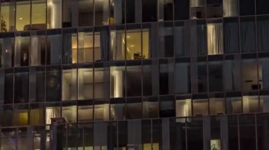 Aydınlatılmış çalışma odası saatleriyle apartman penceresi ön cephesinin gece görüşü. Gökdelende yanıp sönen ışık