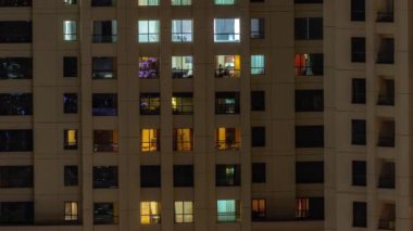 Oturma odalarında parlayan pencereleri olan bir apartman dairesinin akşam manzarası. Işıklı gökdelenle aydınlatılmış yüksek bir gökdelen